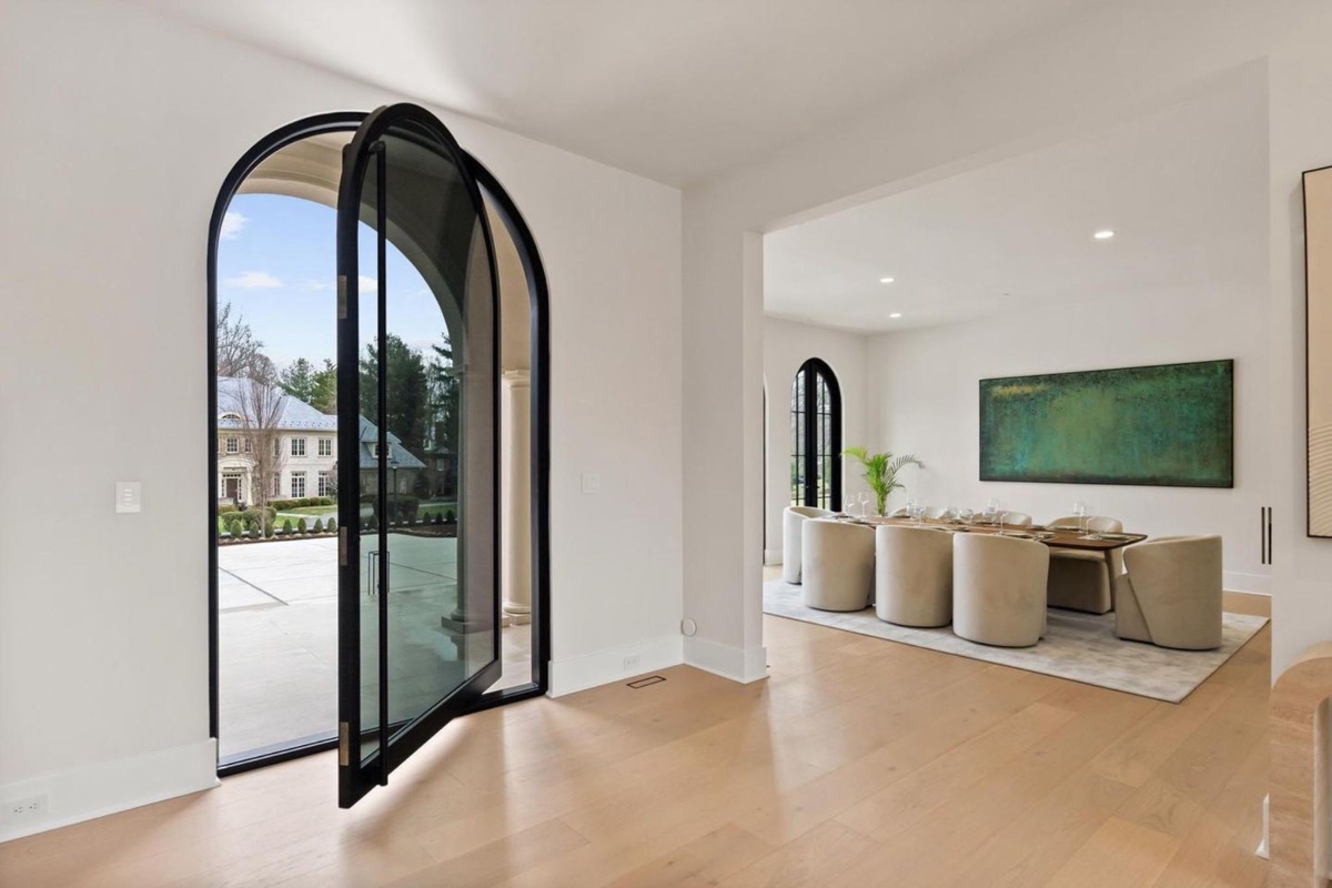 Arched steel and glass pivot entry door opening onto white oak floors